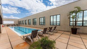 Uma piscina no terraço com vista clara para o horizonte da cidade, rodeada por um edifício de tijolo com grandes janelas e espreguiçadeiras.