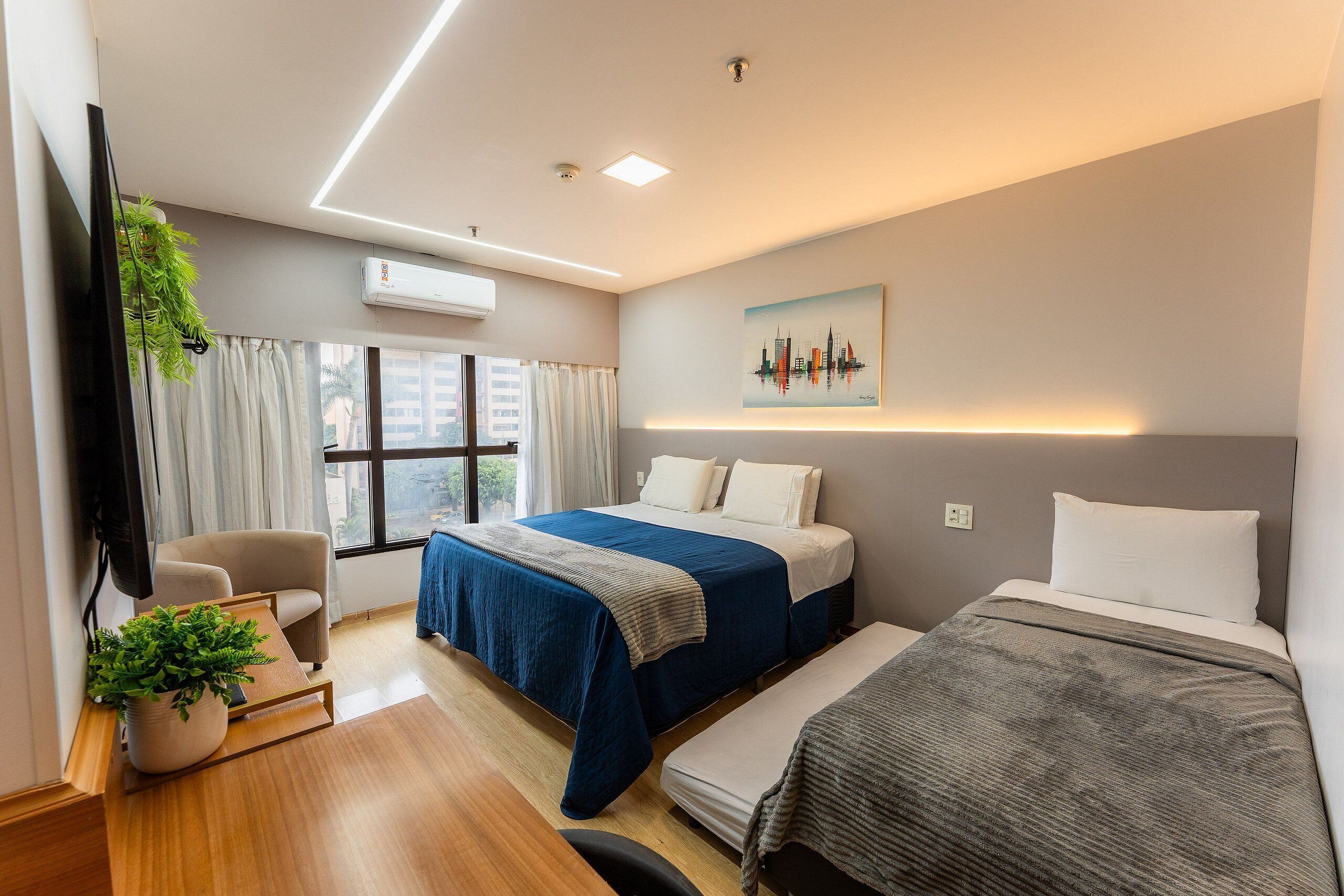 Una habitación de hotel moderna con dos camas, un escritorio, una silla, un televisor y un ventanal con cortinas.