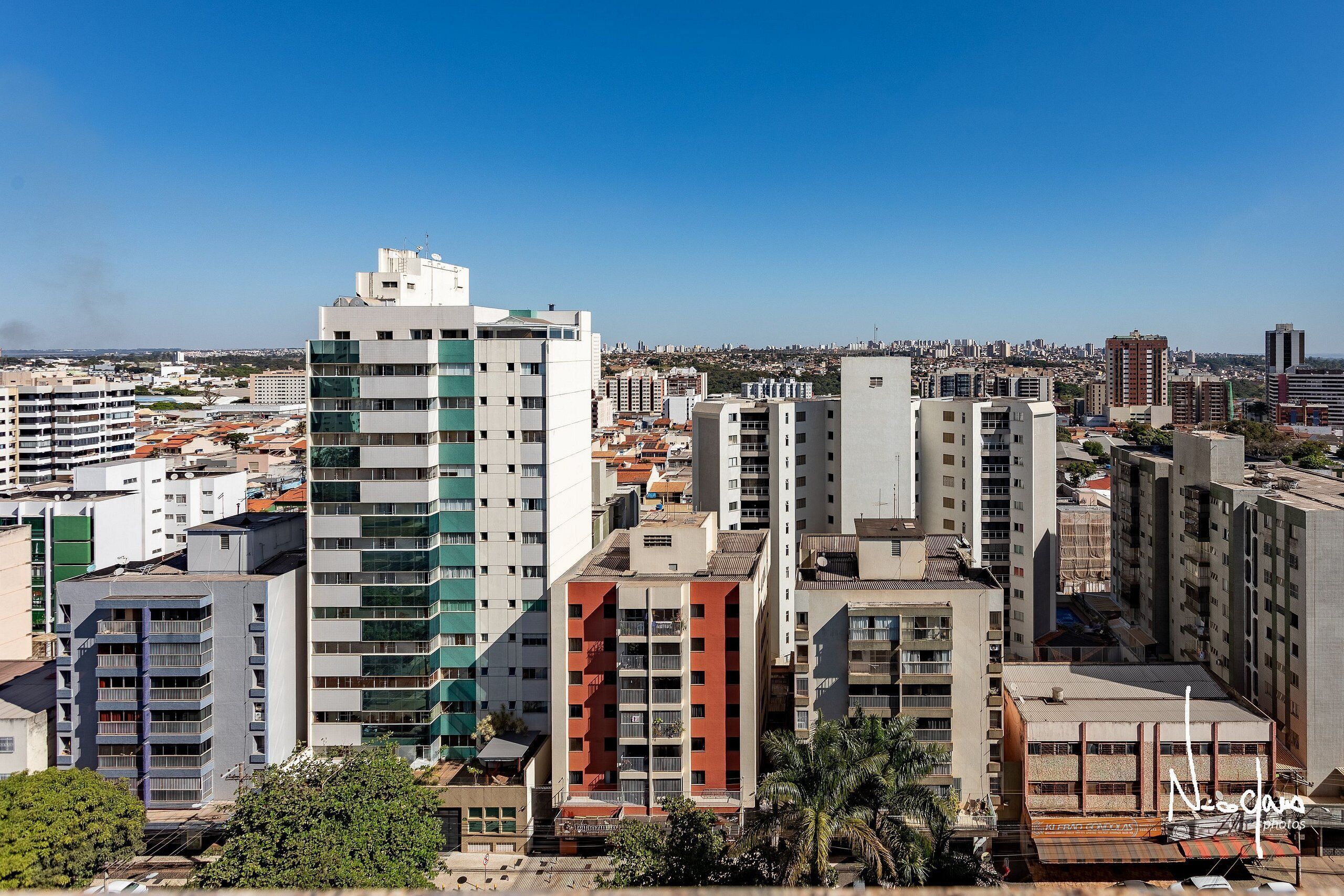 A cityscape with various buildings, including a prominent white building with green accents and a red building with balconies.