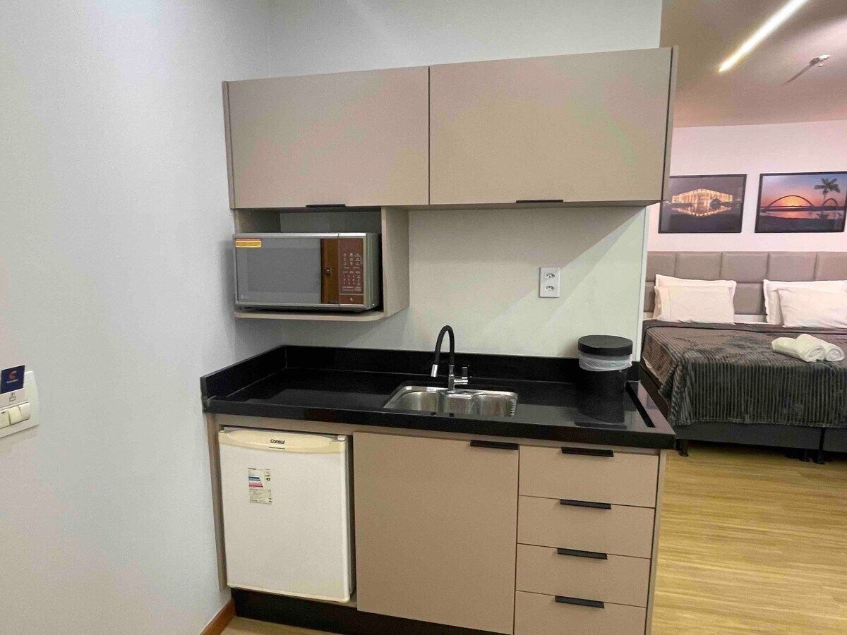 Una kitchenette compacta con microondas, pileta y heladera pequeña.
