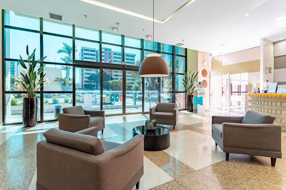 A modern hotel lobby with large windows, comfortable seating, and a reception area.