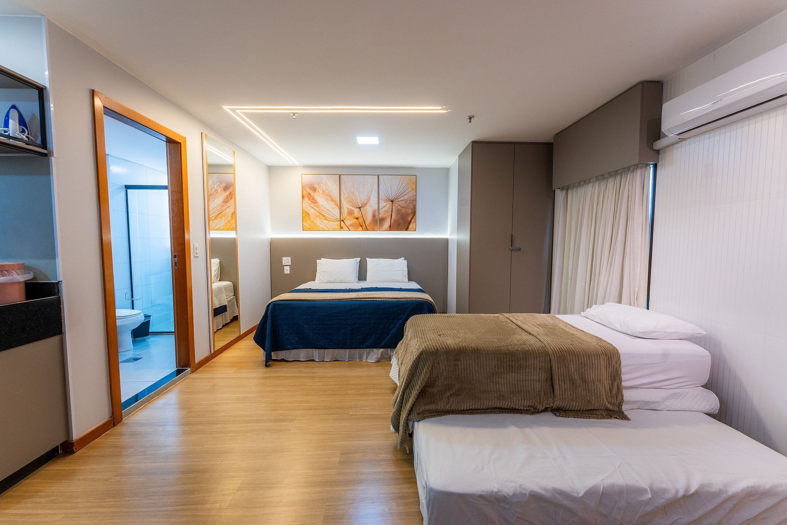 Una habitación de hotel con piso de madera, una cama con cubrecama azul, una mesita de noche y un ventanal con cortinas.