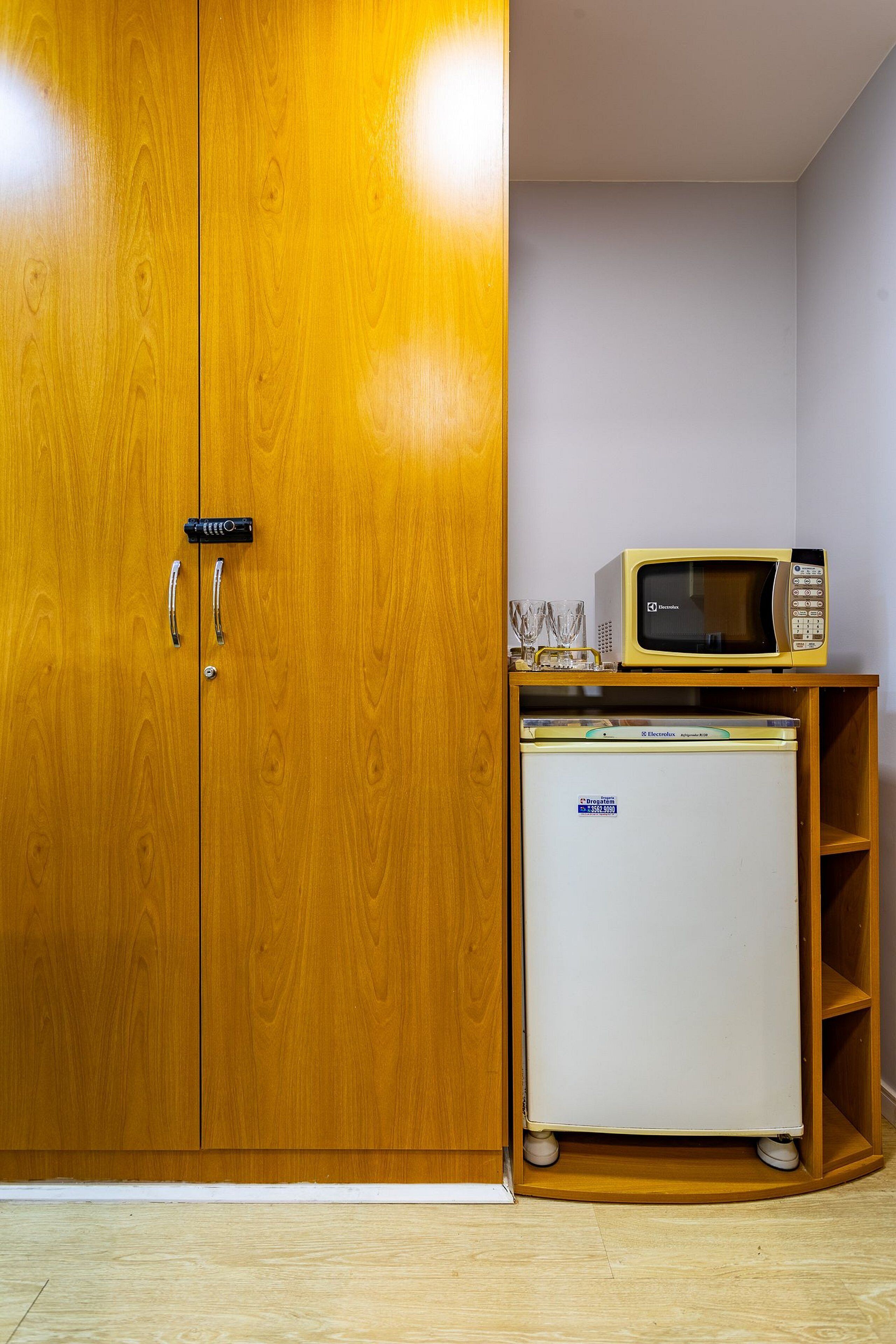 Un armario de madera con dos puertas, un refrigerador blanco pequeño y un microondas encima de un estante de madera.