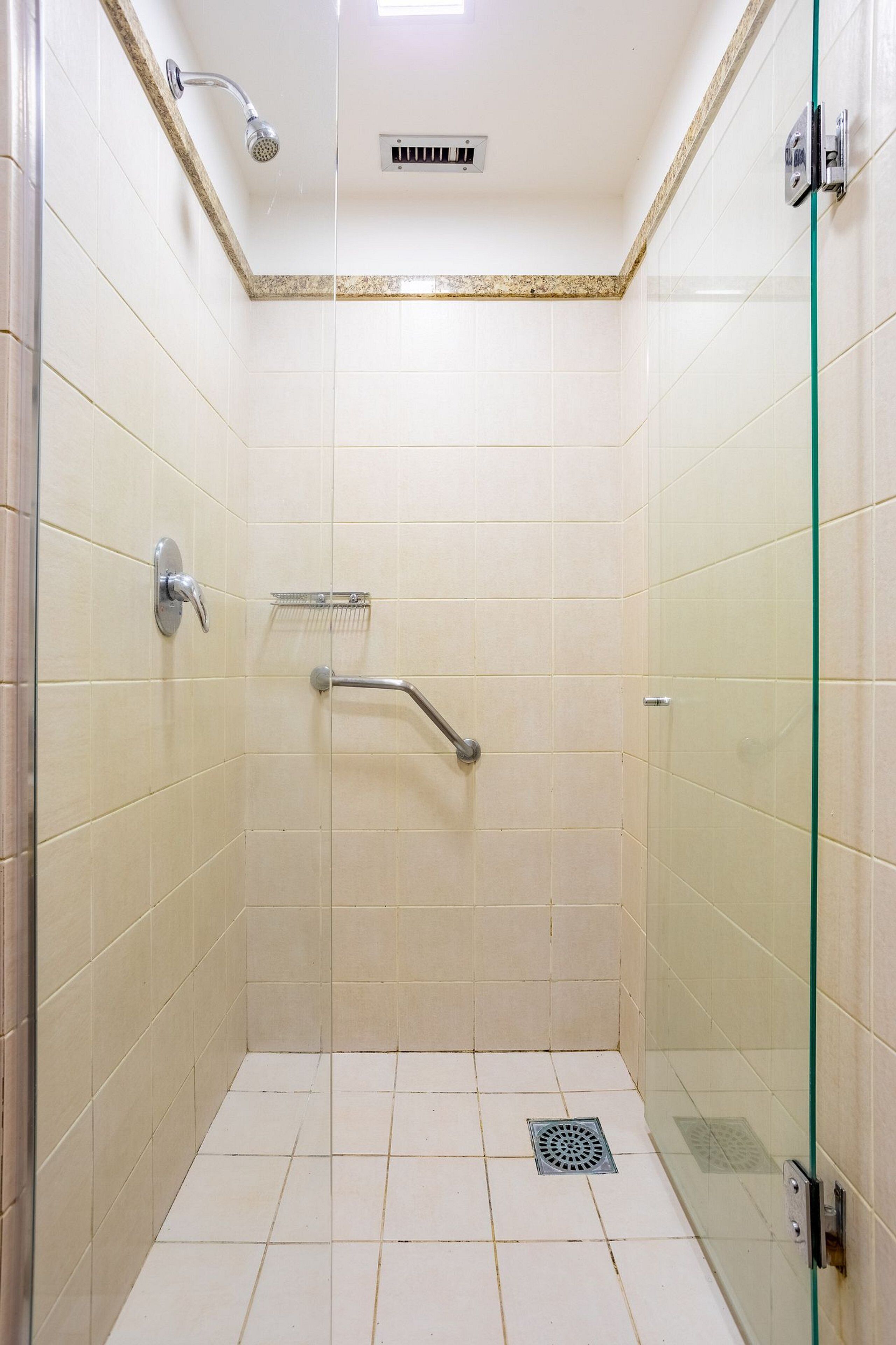 A small, enclosed shower area with a glass door, a handheld showerhead, a handheld shower control, and a floor drain.
