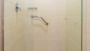 A small, enclosed shower area with a glass door, a handheld showerhead, a handheld shower control, and a floor drain.