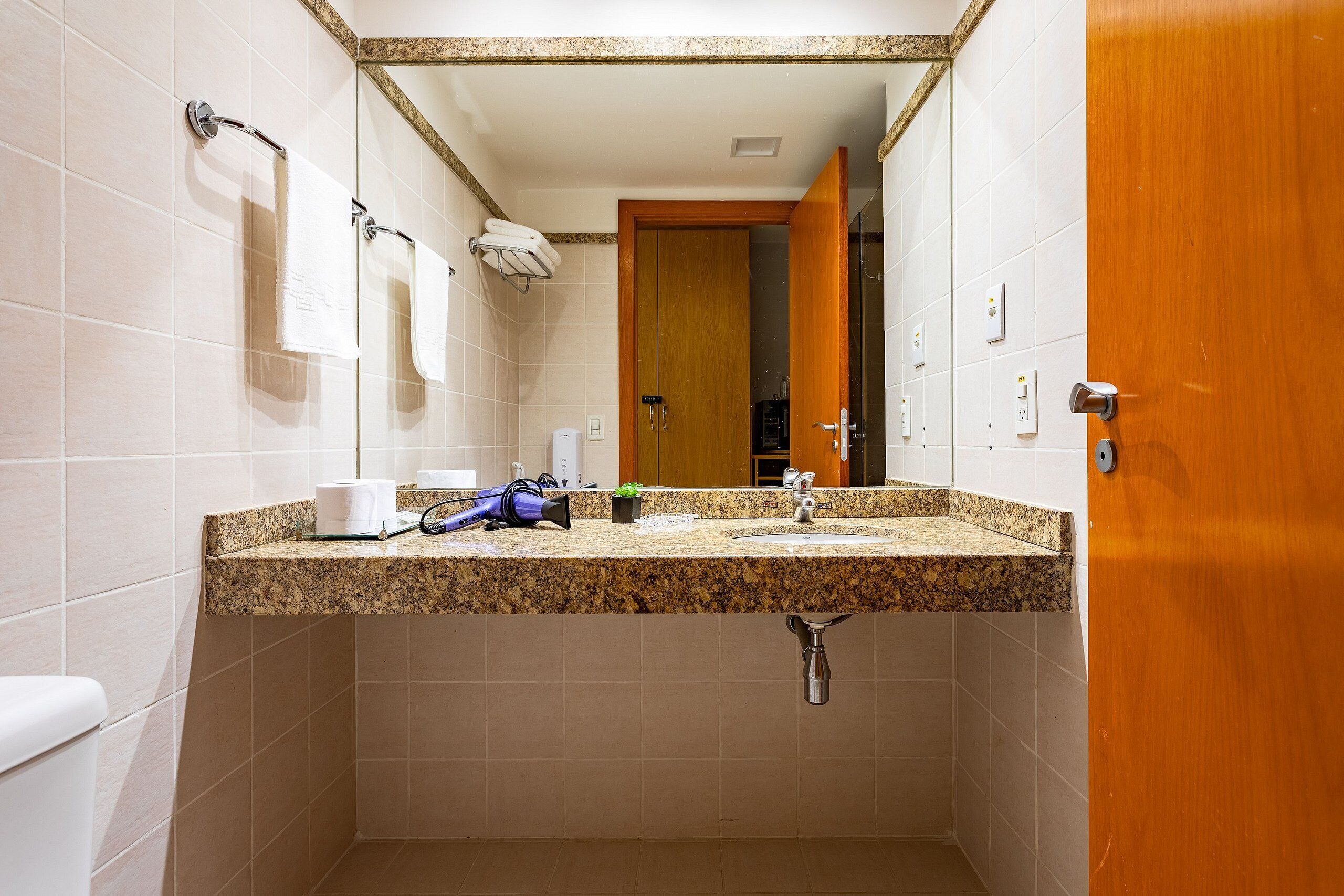 Un baño con encimera de granito, un lavabo, un espejo y un perchero para toallas.