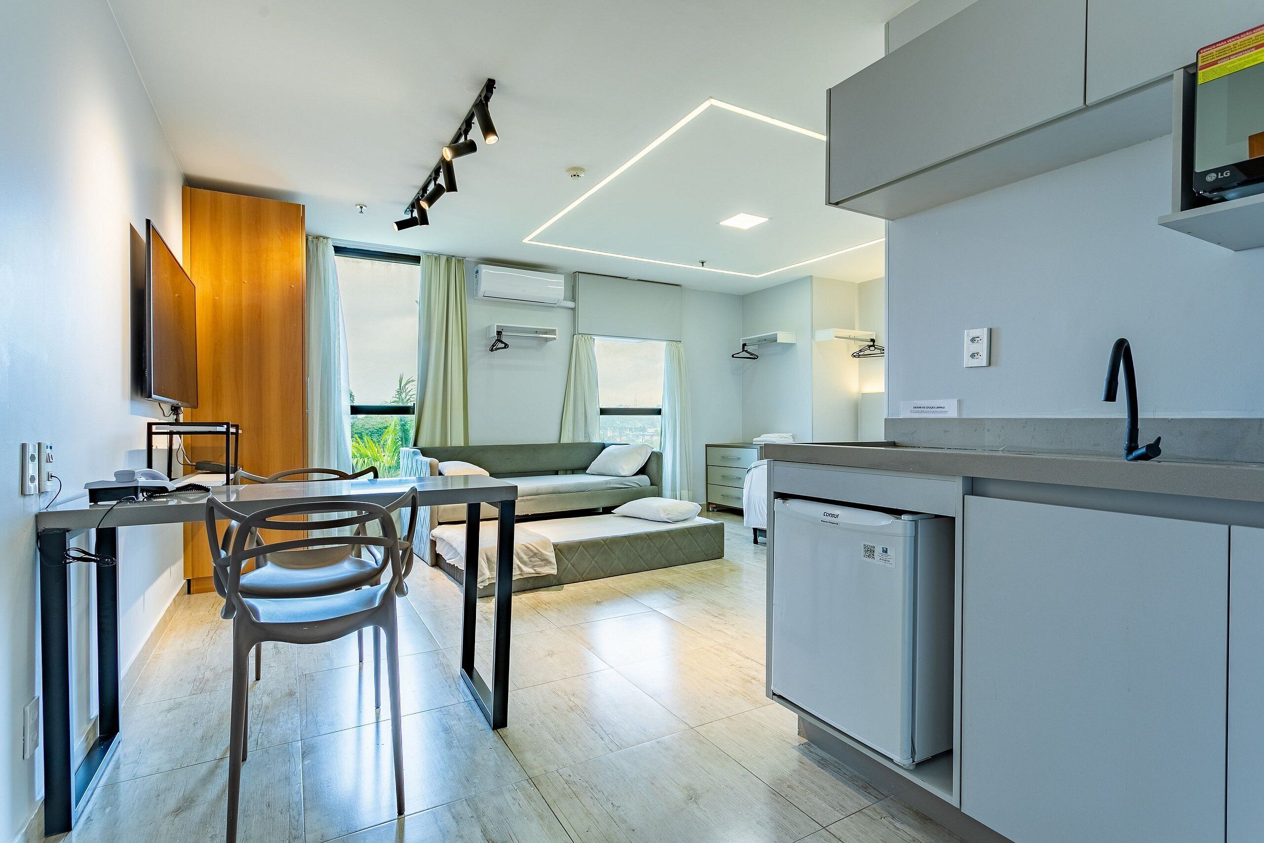 A modern kitchen with a built-in dishwasher, a dining area with a table and chairs, and a sofa in the background.