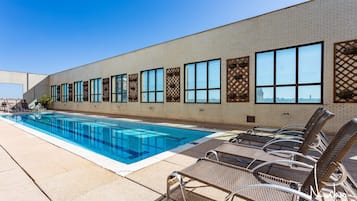Una piscina con sillas de descanso y un edificio de ladrillo con amplias ventanas.