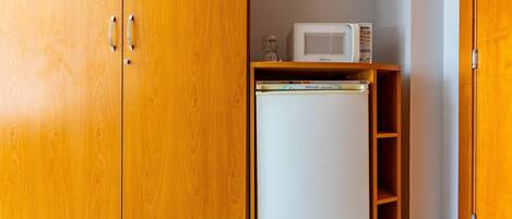 A wooden wardrobe with two doors, a small white refrigerator, and a microwave on top.