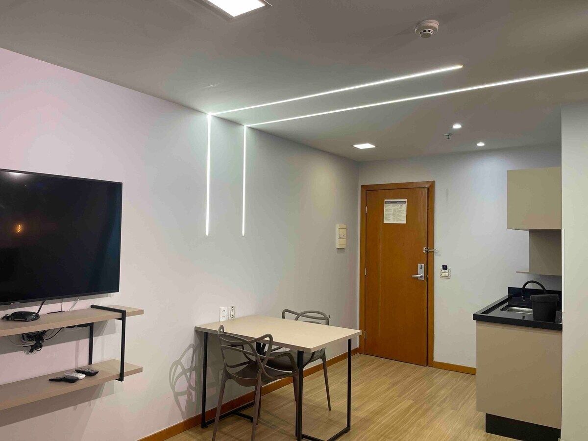 Una habitación moderna con televisión de pantalla plana, una mesa de comedor con sillas, una puerta de madera y una zona de kitchenette.
