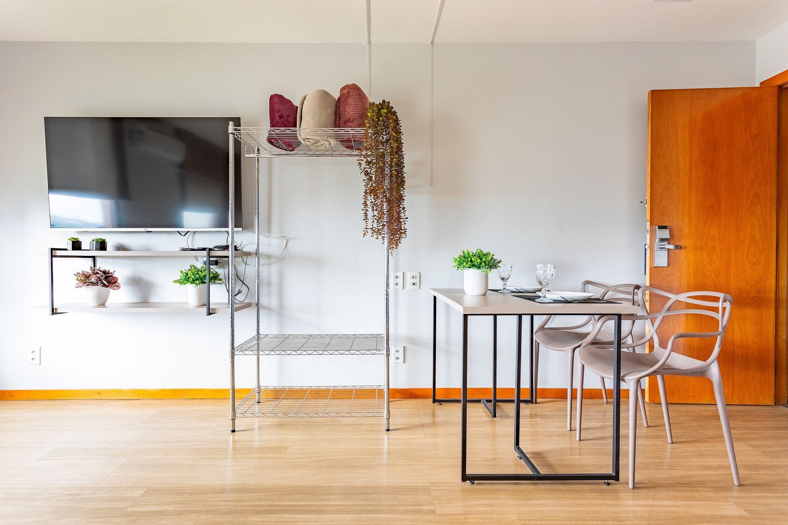 A modern kitchen with a dining area, a TV mounted on the wall, and a wooden door.