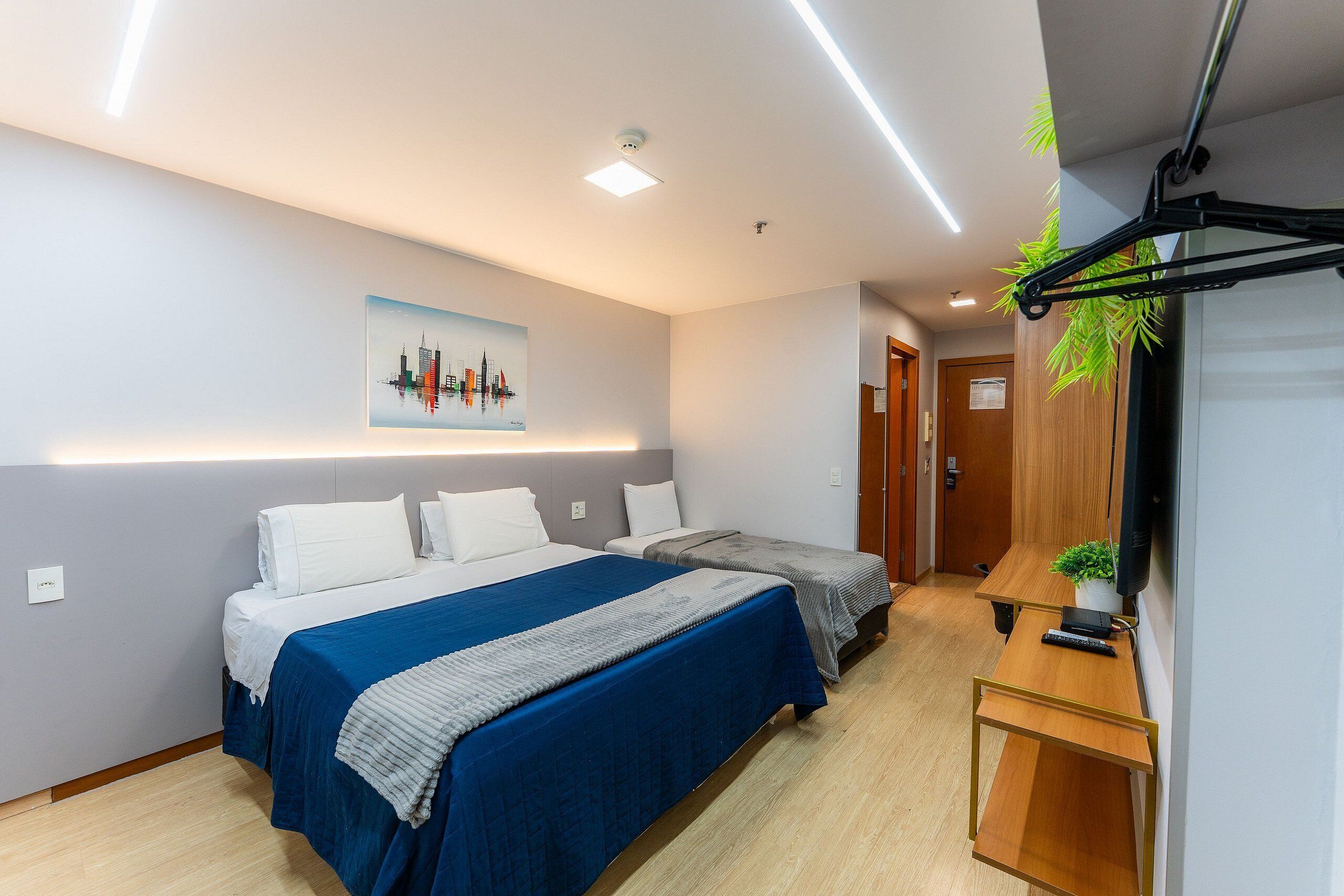 A hotel room with two beds, a desk, a TV, and a cityscape painting on the wall.