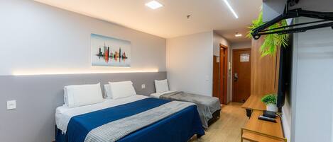 A hotel room with two beds, a desk, a TV, and a cityscape painting on the wall.