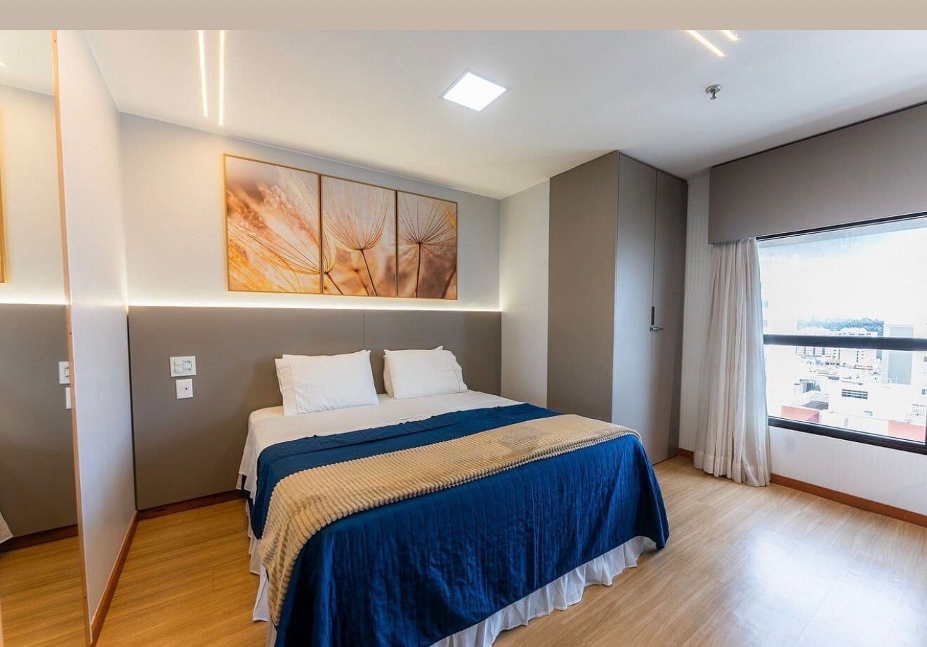 Ein Hotelzimmer mit einem Bett, einem großen Fenster mit Vorhängen, einem Wandbild und einer Deckenleuchte.