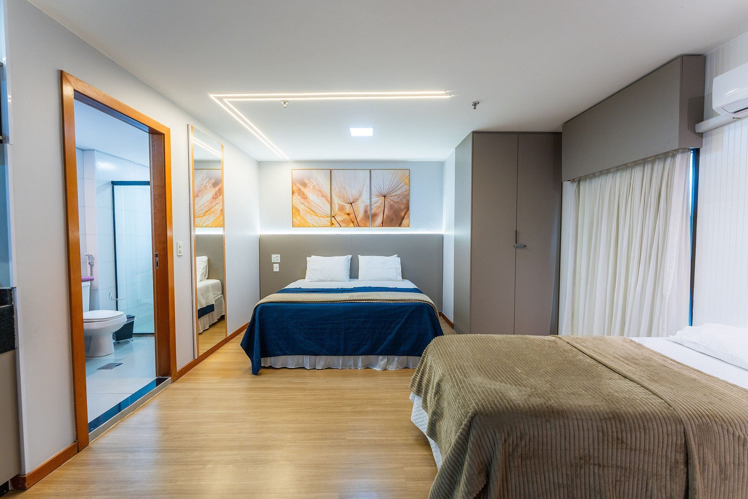 A hotel room with a large bed, a smaller bed, a bathroom with a toilet and sink, and a large window with curtains.
