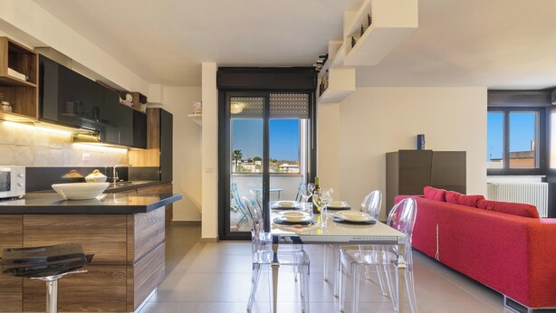 A modern kitchen with a central island, dining area with clear chairs, and a red sofa. - 4021 Casa Dolce Margherita by Barbarhouse (Casarano)