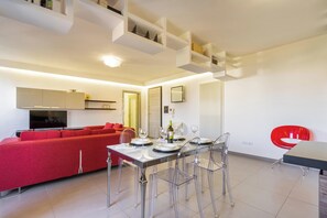 A modern living room with a red sofa, a dining table with clear chairs, and a kitchen area with white cabinets and a TV. - 4021 Casa Dolce Margherita by Barbarhouse (Casarano)