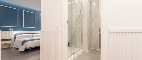 Un baño moderno con cabina de ducha de vidrio, una cama con ropa de cama blanca y una pared de acento azul.