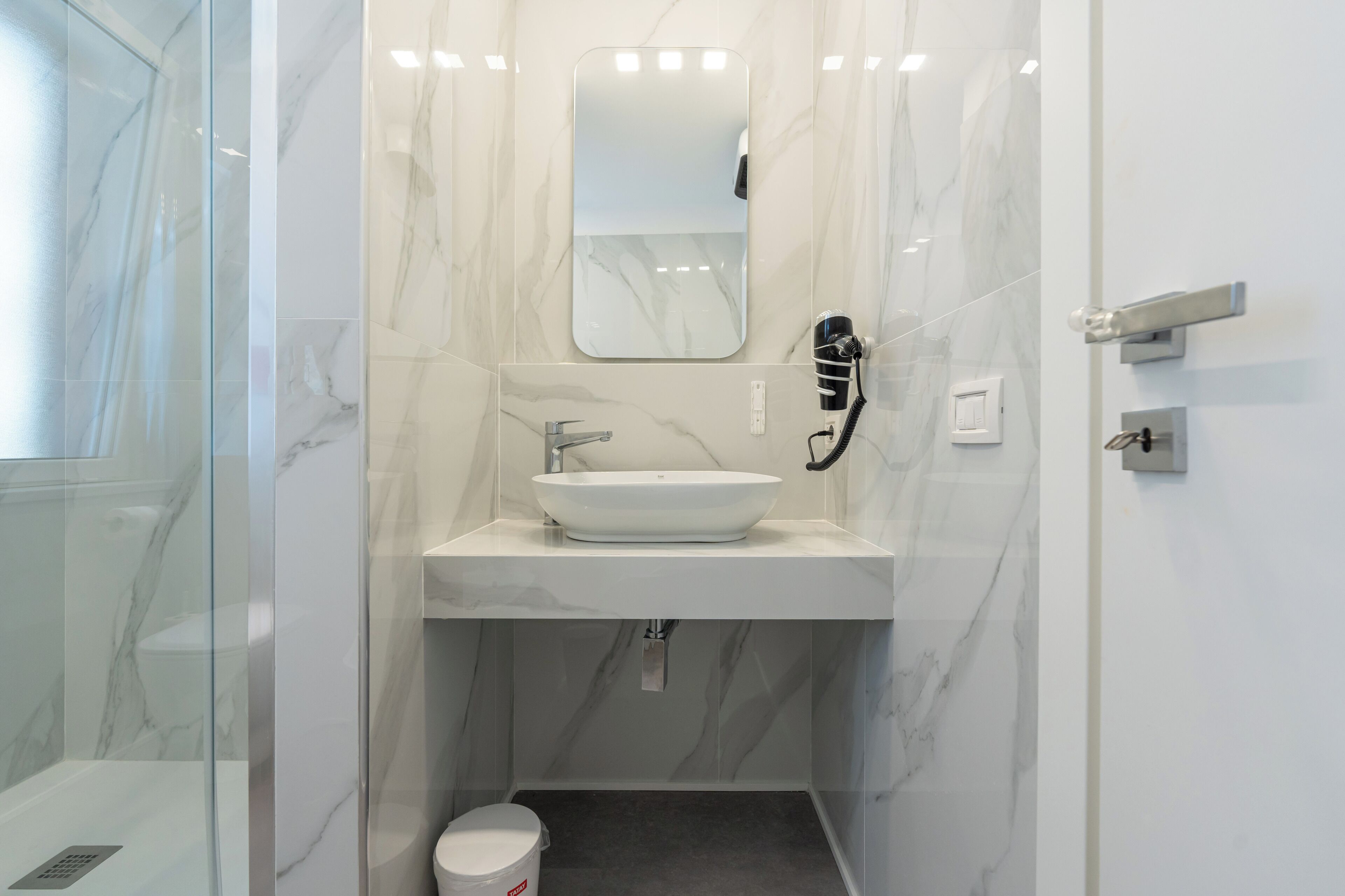 Une salle de bain avec un lavabo blanc, un miroir et un sèche-cheveux fixé au mur.