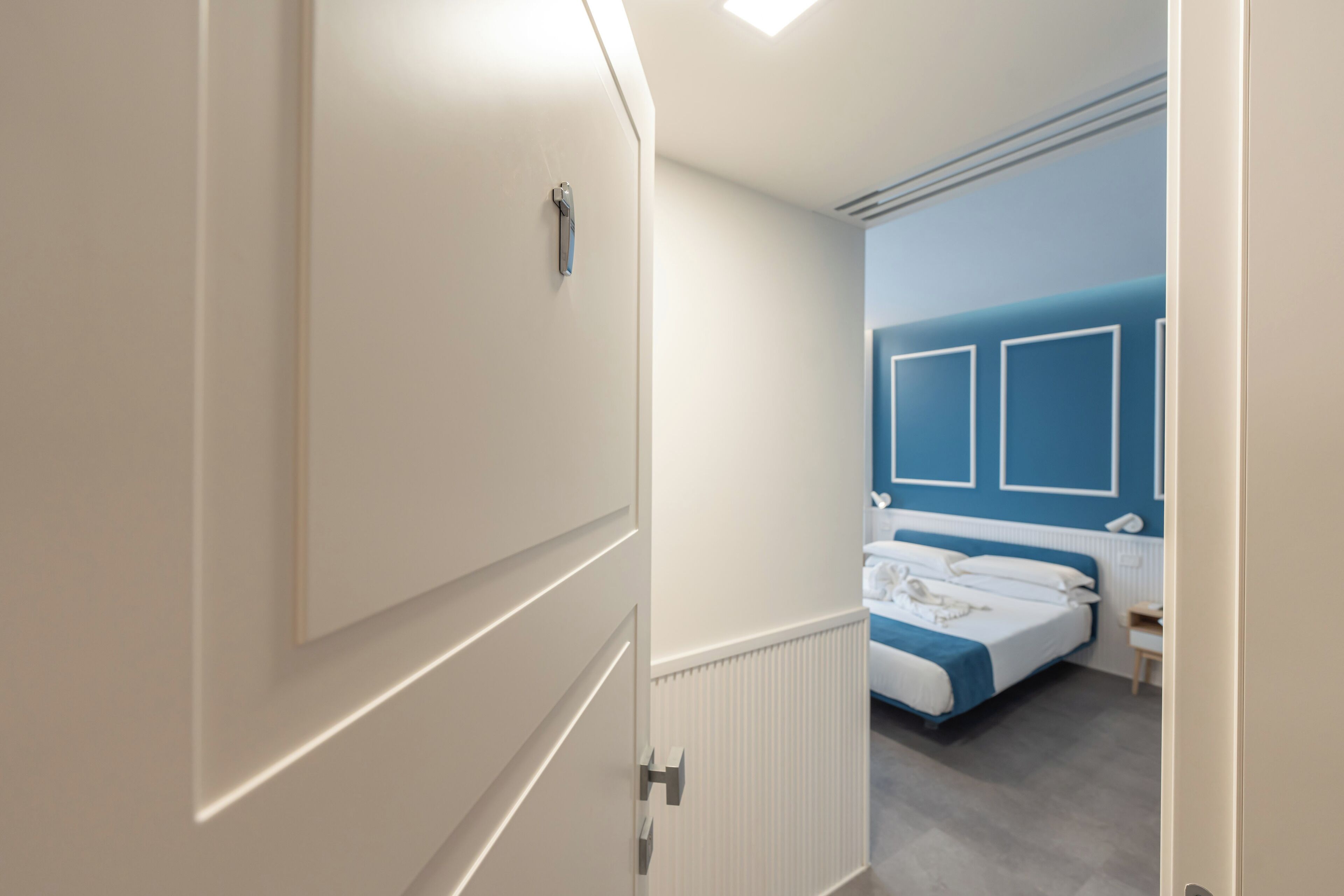 Quarto de hotel moderno com uma cama grande, mesa de cabeceira e guarda-roupa.
