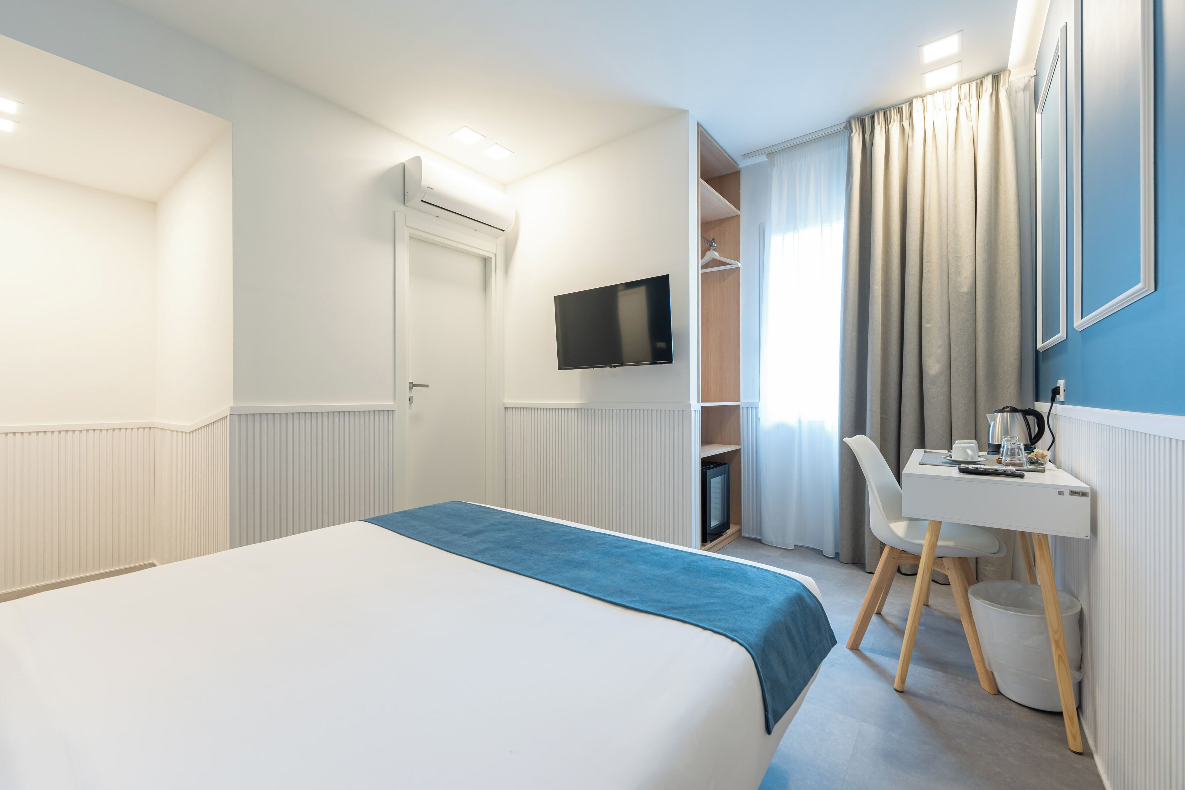Una habitación de hotel con una cama, un escritorio con una silla, un televisor y un armario.