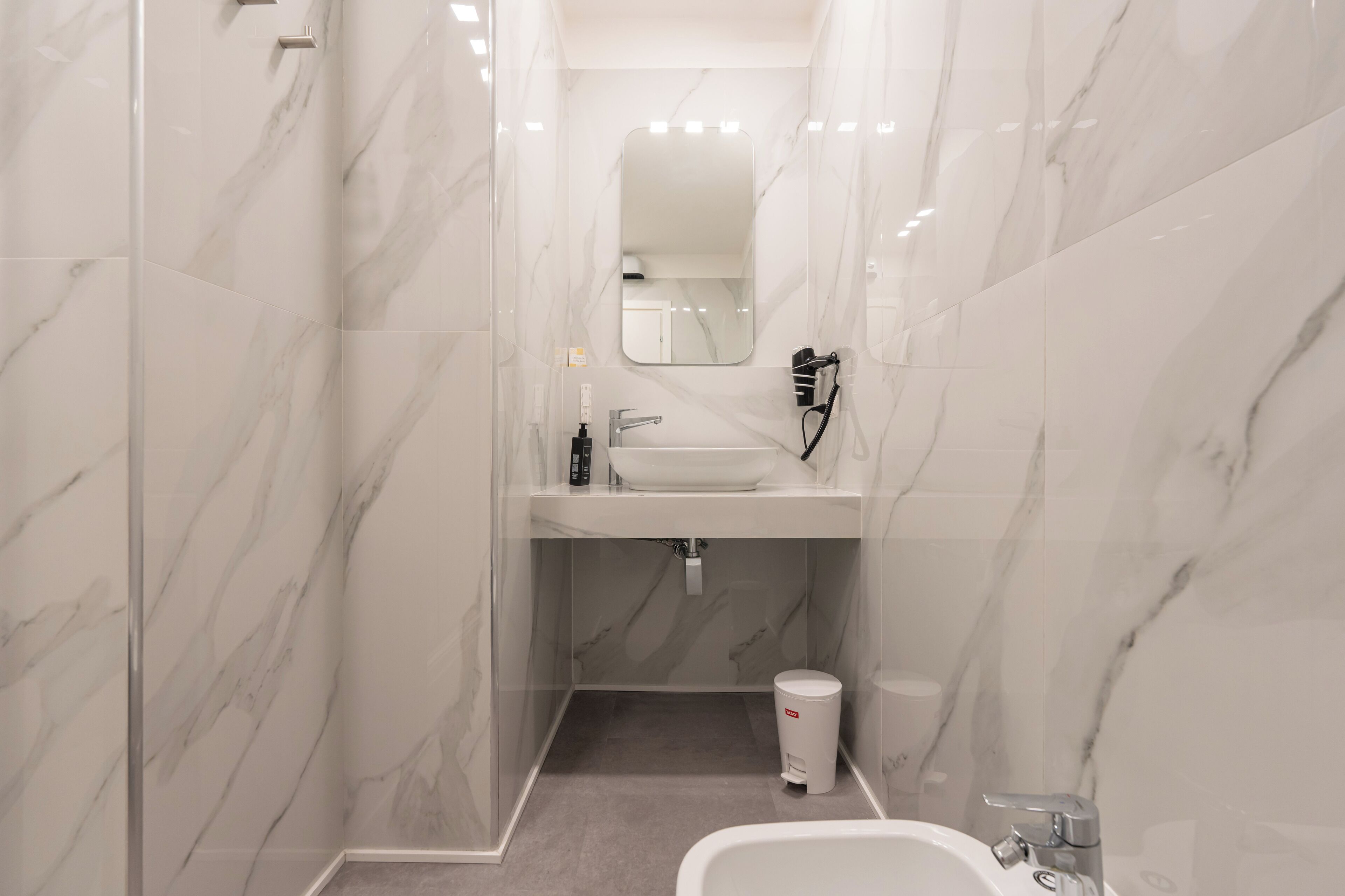 A modern bathroom with a marble floor, a sink, a mirror, and a shower area.