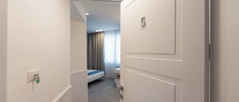 Habitación de hotel con cama, escritorio y vista al pasillo.