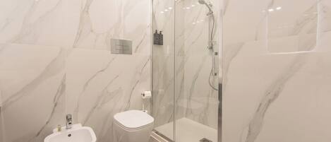 A bathroom with a marble wall, a glass-enclosed shower, a toilet, and a bidet.