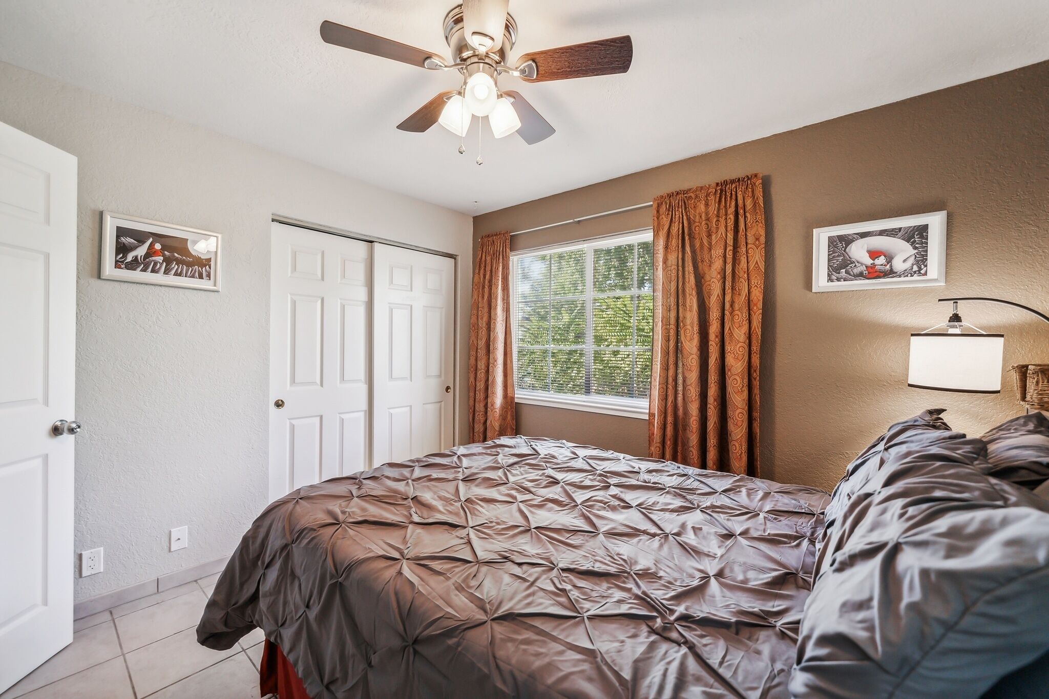 A bedroom with a bed, a ceiling fan, a window with curtains, and a door.