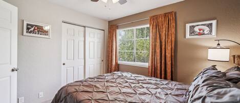 A bedroom with a bed, a ceiling fan, a window with curtains, and a door.