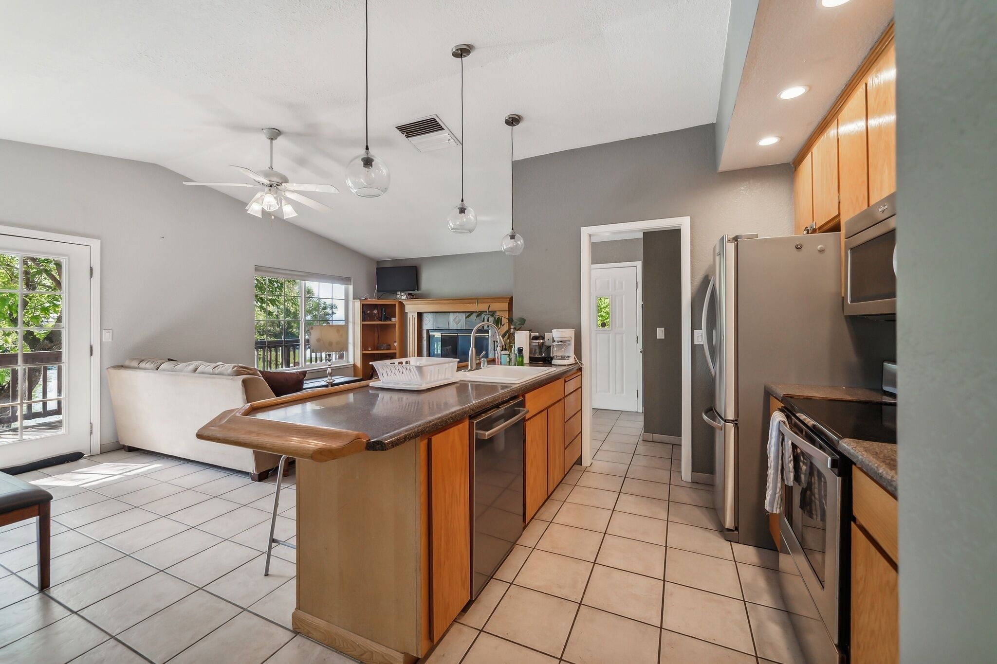 A modern kitchen with wooden cabinets, a central island, stainless steel appliances, and pendant lighting.