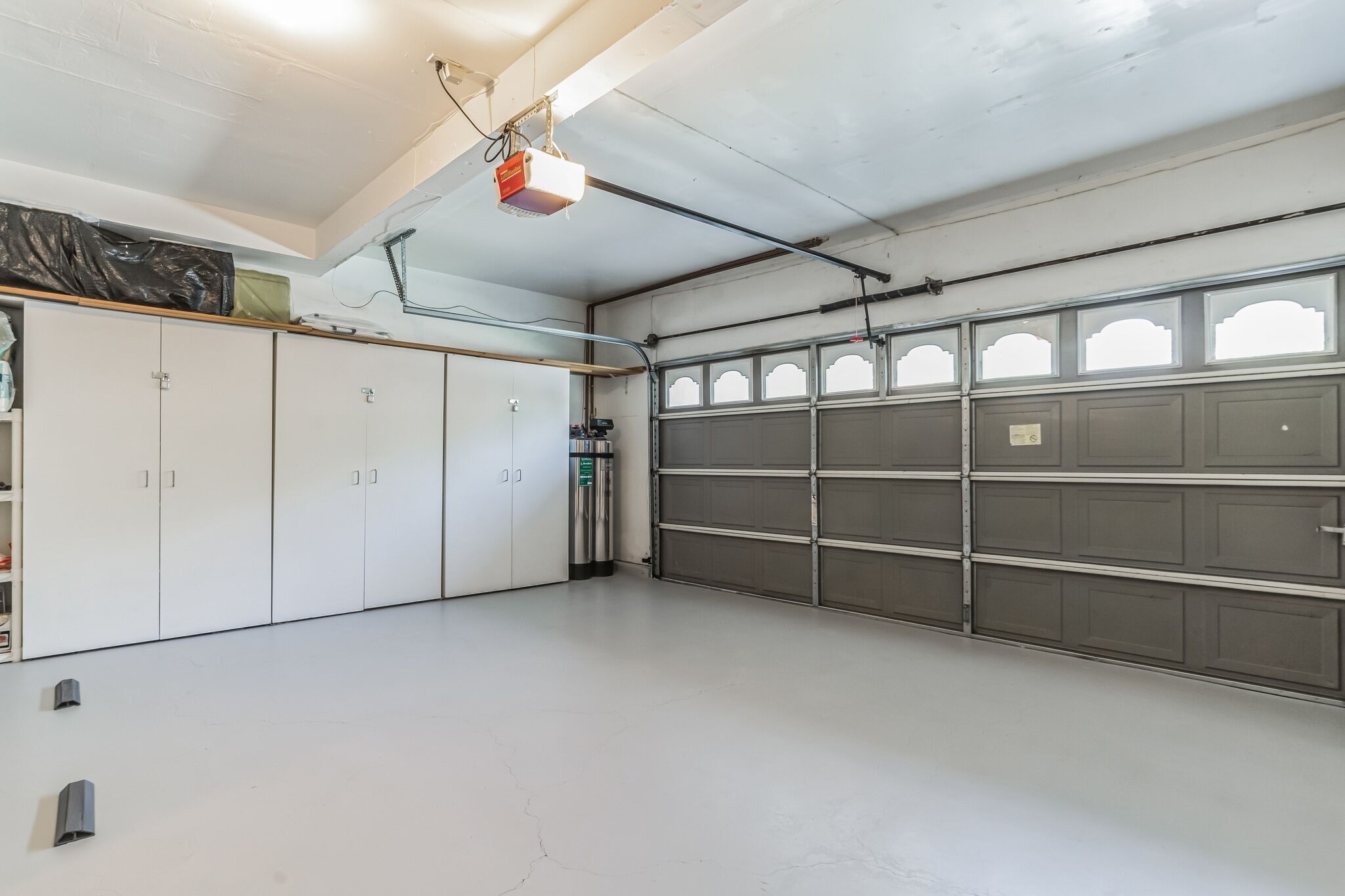 En garage med hvide skabe, en grå garagedør og en projektor monteret i loftet.