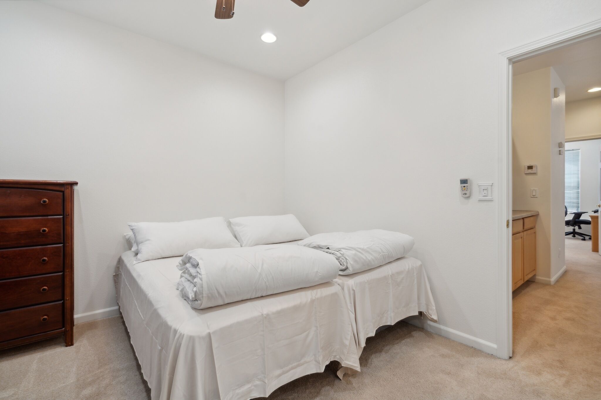 A bedroom with a bed, a wooden dresser, and a door leading to another room.