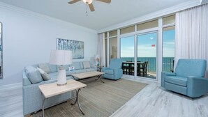 A modern living room with a sofa, two armchairs, a coffee table, and a large window with a view of the ocean. - Phoenix Orange Beach 804 3 Bedroom Condo (Orange Beach)