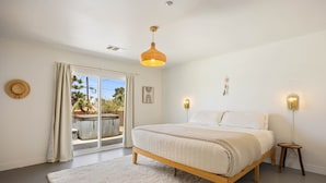 Une chambre avec un lit, un luminaire suspendu, une table de chevet et une vue sur une piscine, visible à travers une porte coulissante.