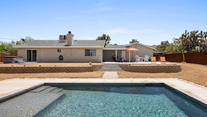 Une maison avec une piscine, une terrasse avec des chaises et un espace couvert.
