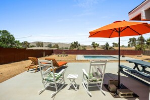 Un patio trasero con piscina, dos mecedoras, una mesa de picnic y un paraguas naranja.