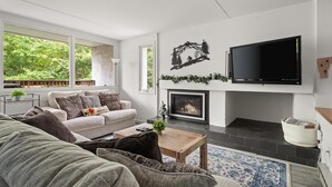 Una sala de estar moderna con chimenea, un televisor de pantalla plana y un amplio ventanal con vistas a zonas verdes.