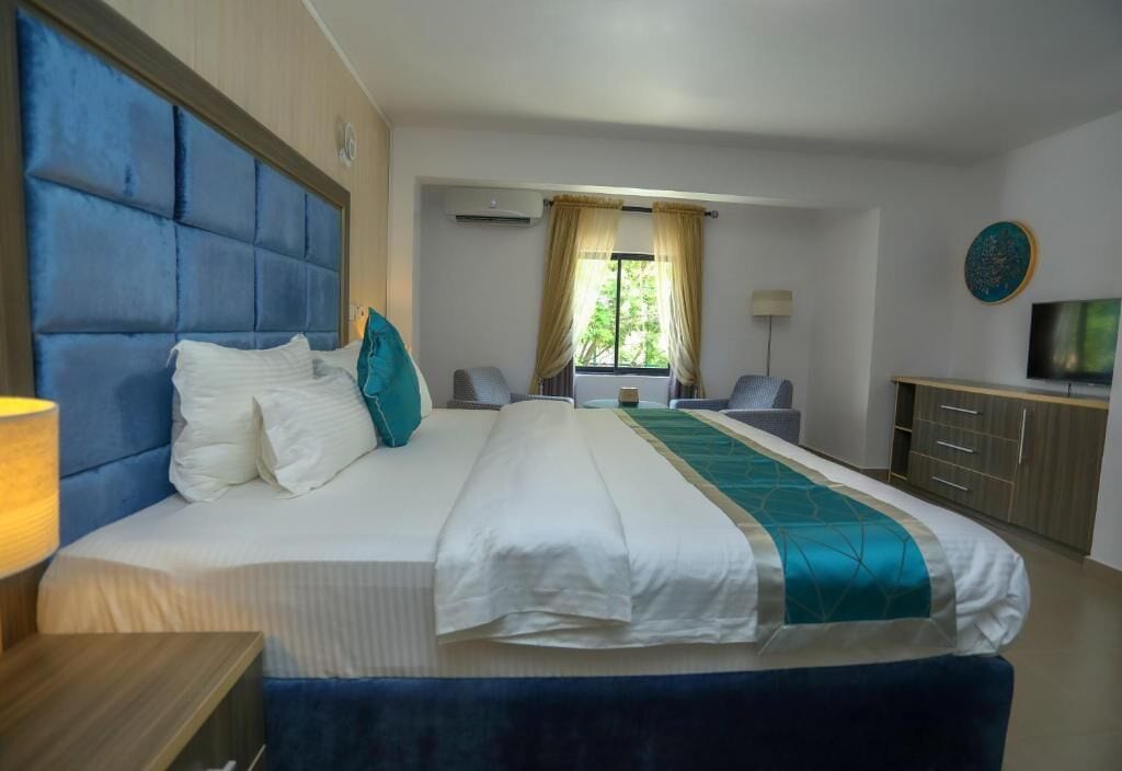 A hotel room with a large bed, a desk, a chair, a TV, and a window with curtains.