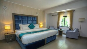 A hotel room with a large bed, two bedside tables with lamps, a chair, a small table, and a window with curtains. - Riviera Luxury Boutique Hotel (Lagos)