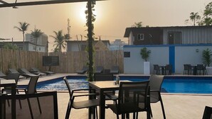 A poolside area with lounge chairs and a table, surrounded by a bamboo fence and palm trees. - Riviera Luxury Boutique Hotel (Lagos)