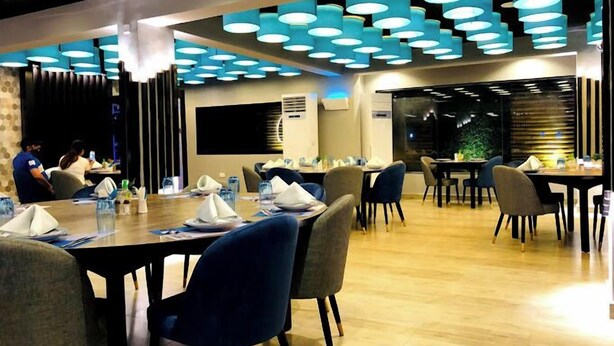 A modern restaurant with round tables, blue chairs, and a ceiling with circular light fixtures. - Riviera Luxury Boutique Hotel (Lagos)