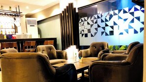 A modern lounge area with leather sofas and a wooden coffee table, a bar with bottles, and a geometric wall design. - Riviera Luxury Boutique Hotel (Lagos)