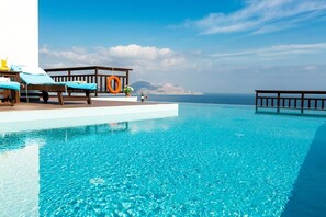 A clear blue infinity pool with lounge chairs and a wooden deck overlooking the sea. - Almirida Infinity Resort – Stylish Villa with Pool (Almirida)