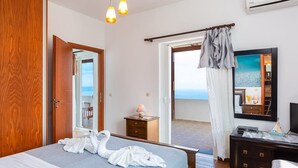 A hotel room with a bed, a bedside table with a lamp, a dresser, a TV, and a balcony with a view of the sea.