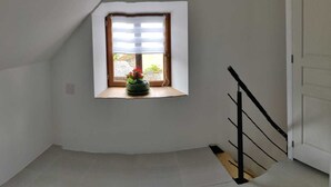 A small, sloped room with a window, a wooden floor, and a black railing. - Small house in the heart of a 15th century property. (Huillé-Lézigné)