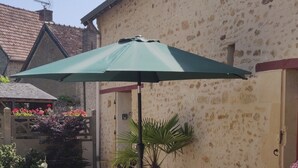 A patio with a table and chairs under a green umbrella, surrounded by gravel and potted plants. - Small house in the heart of a 15th century property. (Huillé-Lézigné)