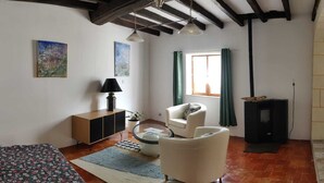 A living room with a sofa, armchair, and a small table. There is a lamp, a cabinet, and a window with curtains. - Small house in the heart of a 15th century property. (Huillé-Lézigné)