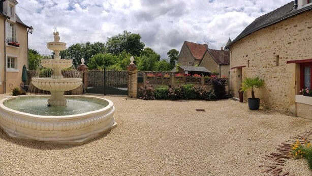 A courtyard with a multi-tiered fountain, stone buildings, and potted plants. - Small house in the heart of a 15th century property. (Huillé-Lézigné)
