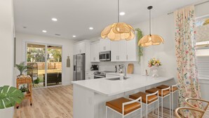 Une cuisine moderne avec des meubles blancs, un îlot central doté de tabourets et des luminaires suspendus.